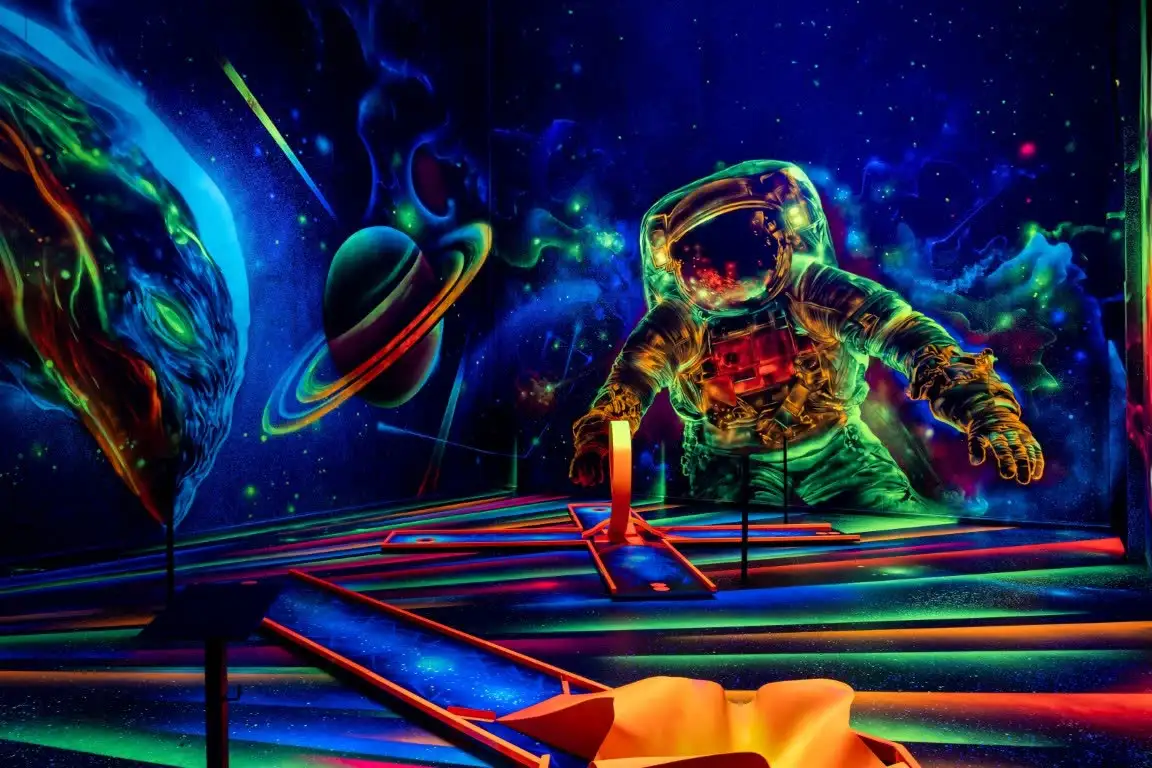 Ein riesiger leuchtender Astronaut an der Wand, daneben ein Ringplanet, davor die Minigolfbahnen.